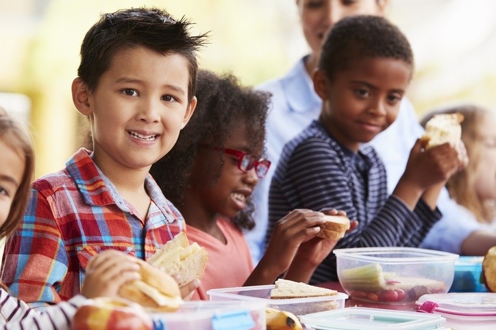 School kids eating packed lunches together at a table