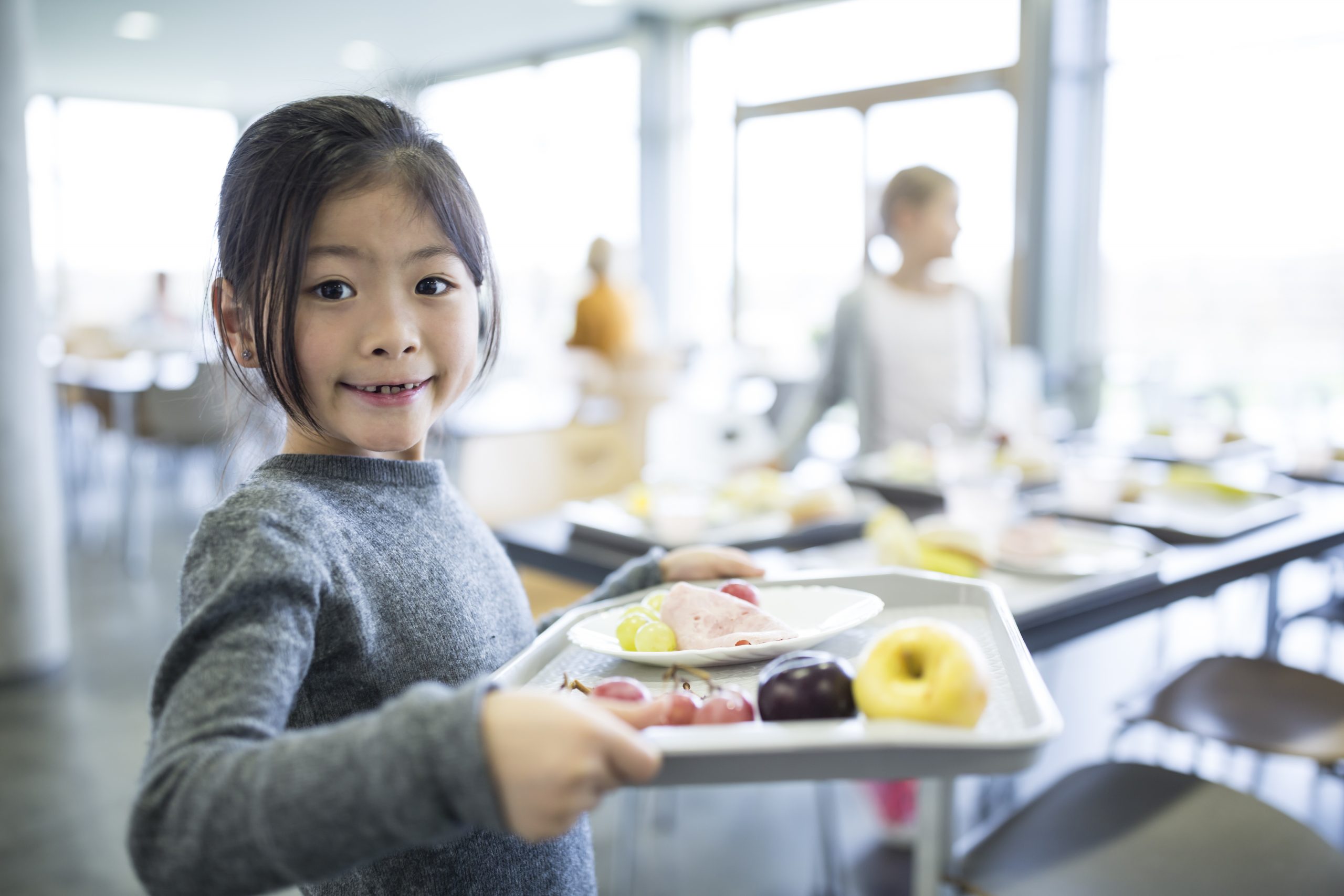 Portrait of smiling schoolgirl carrying tray in school canteen
