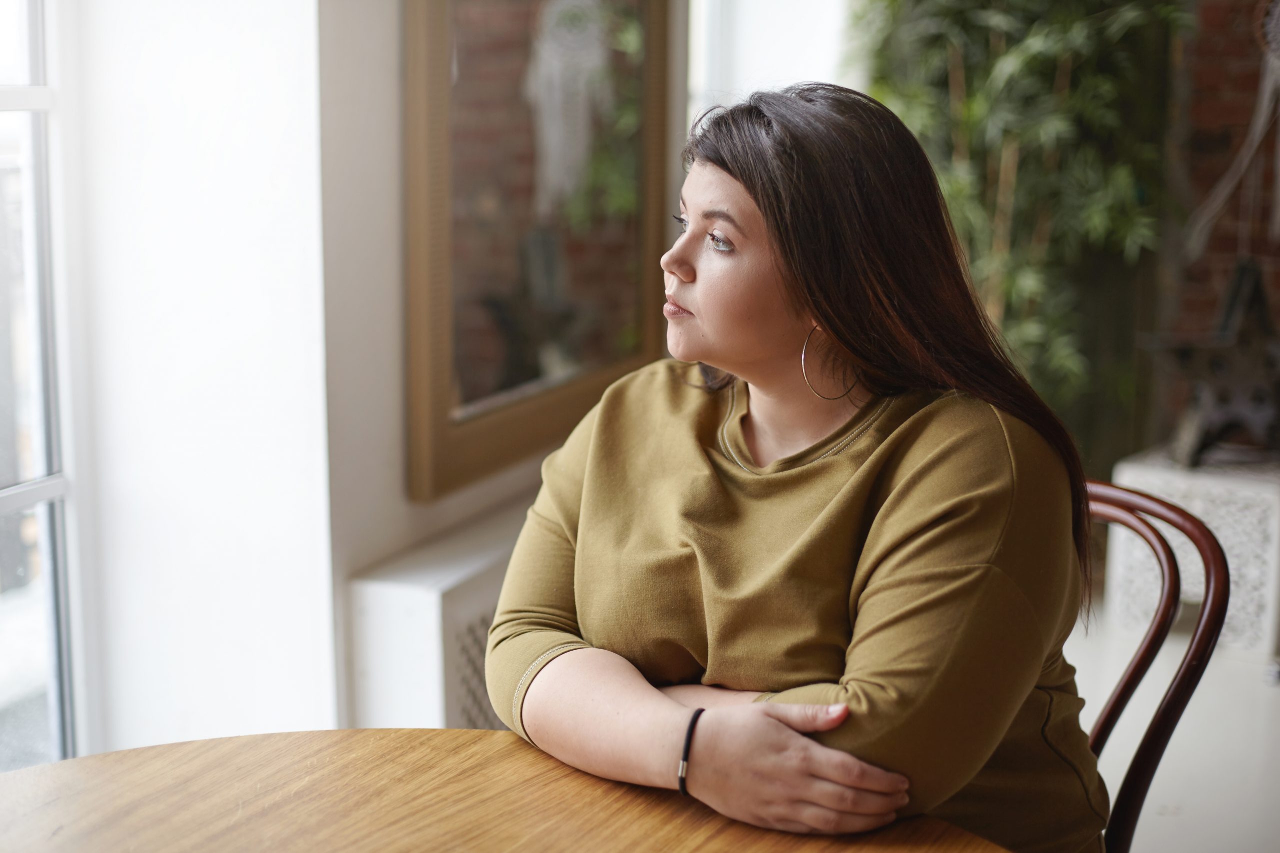 Young woman sitting at table tarting out of window.