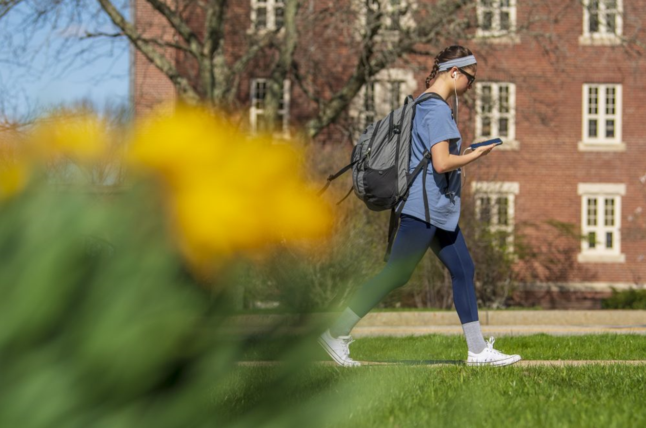 A college student walks across campus looking at a phone; credit Sean Flynn